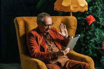 Senior man waving on video call through tablet PC at home