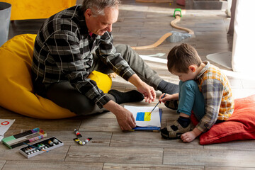Happy grandfather teaching drawing of Ukrainian flag to grandson at home