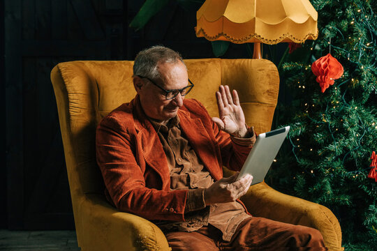 Senior man waving on video call through tablet PC at home