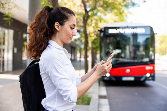 Businesswoman using smart phone standing in front of bus