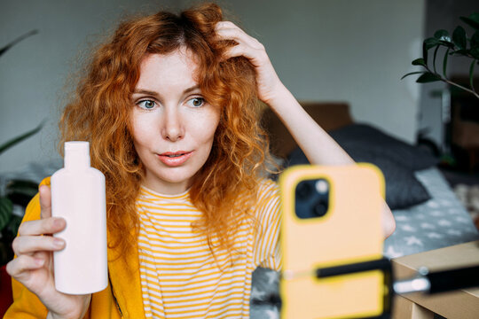 Red haired woman blogger broadcasts live reviews of beauty products for hair