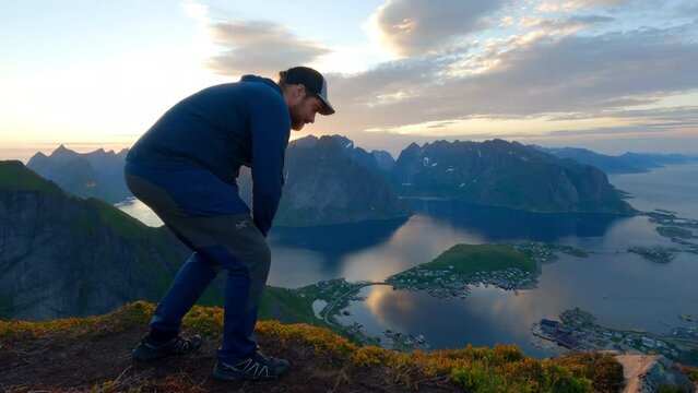Tourist sitting on the top of Reinbringen in Lofoten and enjoying the scenic view from above