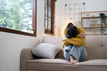 Hand on temples of young unhappy sadness Asian girl sitting on sofa. She is feeling not very good due to her sickness and having a headache. Seen from the front. Stress and sickness concept.