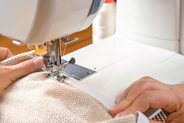 Seamstress hands holding white textile fabric. Female hands stitching white fabric on modern sewing machine at workplace. Close up view of sewing process. Handmade, hobby, small business concept