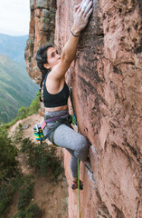 Fit woman rock climbing, stretching arm to hold far away
