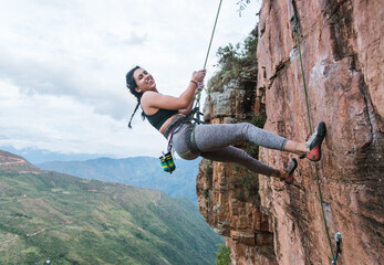 Joyous hispanic rock climber hanging on rope smiling