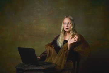 Shocked young charming girl in image of Mona Lisa, La Gioconda using laptop isolated on dark green background. Creative art, beauty, style, imitation, eras comparison