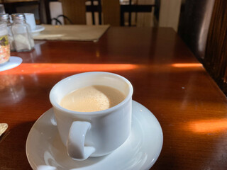 a classic morning coffee in a white cup on wooden table with direct sunlight and shadow