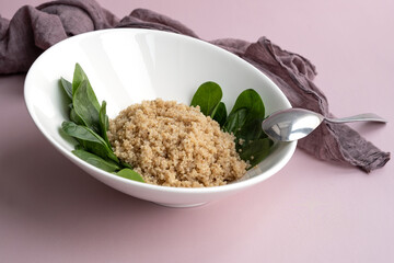 white plate with cooked quinoa and spinach leaves.