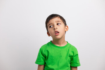 tired boy child in a green T-shirt is having fun on a white background in the studio without baby teeth.