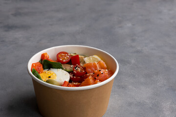 Takeaway poke bowl with fresh salmon, avocado, quinoa and vegetables in recycled kraft paper packaging. Healthy Trendy Fitness food.