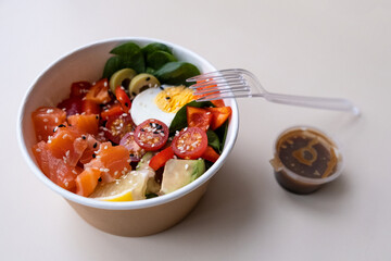 Takeaway poke bowl with fresh salmon, avocado, quinoa and vegetables in recycled kraft paper packaging. Healthy Trendy Fitness food.