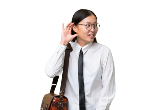 Young Asian business woman over isolated background listening to something by putting hand on the ear