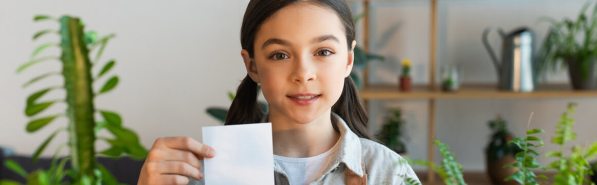 Smiling Kid Holding Sticky Note Near Blurred Plants At Home, Banner.