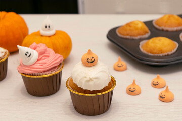 Caucasain woman decorating freshly made cupcakes or maffins with cream at the kitchen