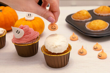 Caucasain woman decorating freshly made cupcakes or maffins with cream at the kitchen