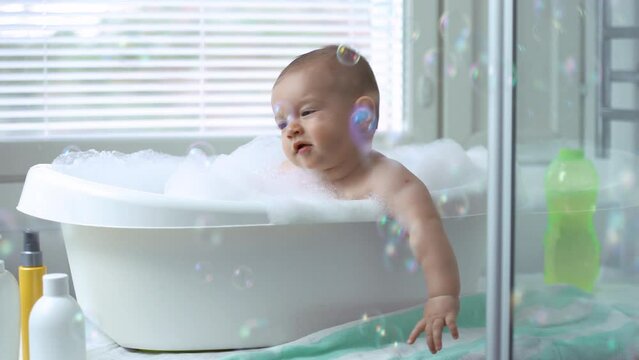 Cute healthy six month old baby bathing with foam and soap bubbles