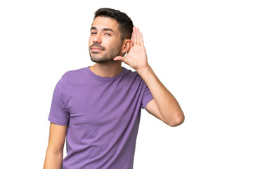 Young handsome caucasian man over isolated background listening to something by putting hand on the...