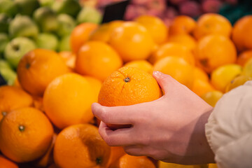 Close-up, woman choosing orange at the grocery store.