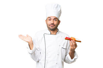 Young caucasian chef holding a sushi over isolated background having doubts while raising hands