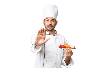 Young caucasian chef holding a sushi over isolated background making stop gesture