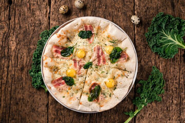 Pizza with quail eggs, baby mozzarella cheese and ham a wooden table. Traditional Italian cuisine