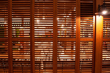 Cafe interior behind wooden shutters. Warm brown colored wooden shatters lighted by electric lamp. Wooden shutter as decorative partition element.