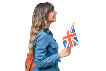 Young caucasian woman holding an United Kingdom flag over isolated background laughing in lateral...