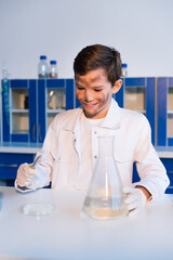 smiling boy with dirty face holding tweezers near petri dish and flask in lab.