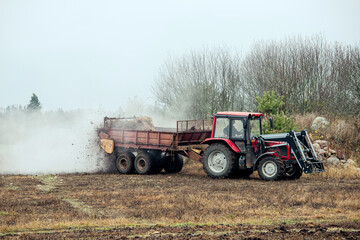 Fototapeta premium Tractor use manure much spreader trailer to scatter hot steaming horse manure on agriculture field in autumn for natural fertilizer.