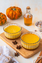 Pumpkin flan, a cold baked dessert of pumpkin puree, eggs, cream and sugar in glass ramekins on a wooden board on a light concrete background. Thanksgiving Day, Halloween