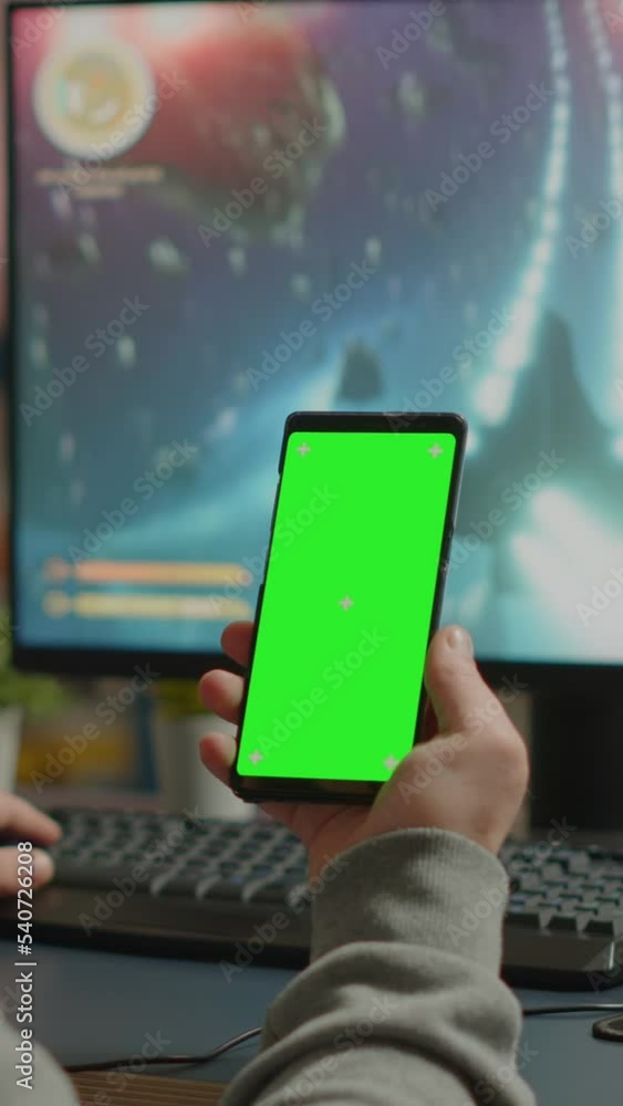 Poster vertical video: concentrate gamer holding phone with green screen mock up chorma key display while p