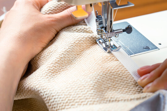 Seamstress hands holding white textile fabric. Female hands stitching white fabric on modern sewing machine at workplace. Close up view of sewing process. Handmade, hobby, small business concept