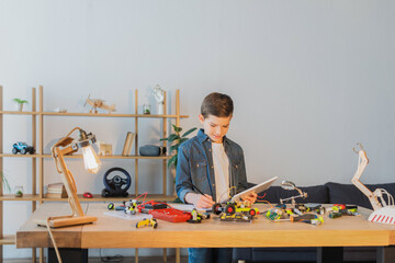 preteen boy holding digital tablet and writing in notebook near mechanical details of robotics model. © LIGHTFIELD STUDIOS