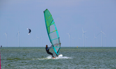 Young woman windsurfing at Ijsselmeer with wind turbines at the horizon (Workum, Netherlands)