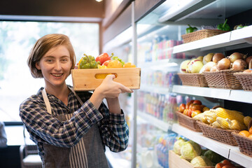 Happy cheerful caucasian grocery store staff arranging a vegetables and fruits on the shelf.