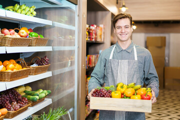 Happy cheerful caucasian grocery store staff arranging a vegetables and fruits on the shelf. 