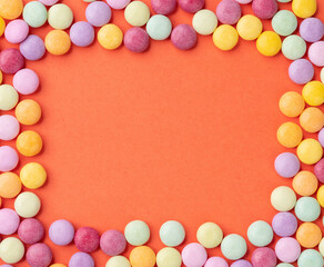 Fototapeta premium Frame of colorful candies over orange background with copy space
