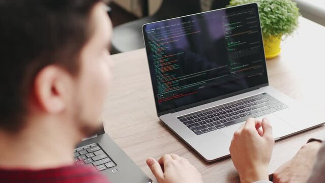 Two hipster coworkers sharing ideas about project sitting with laptops in spacious open space office. Developers discuss application program code. Coder and manager consulting software architecture.
