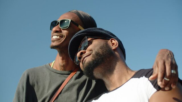 Happy Afro-American gays enjoying summertime together. Close-up shot of cute homosexual man in bandana and sunglasses hugging boyfriends shoulder, looking at each other with love. LGBT, date concept
