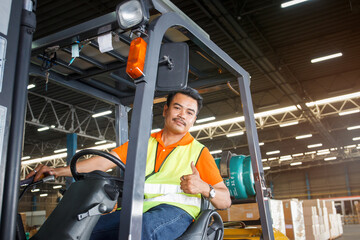 Fototapeta premium Happy and satisfied Asian worker in warehouse sitting a forklift and showing a thumb up to camera.