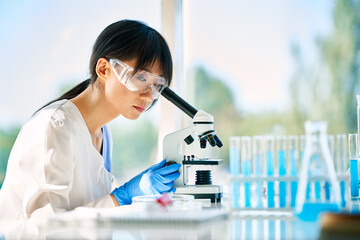 Portrait of asian scientist looking through a microscope working on medical research in modern laboratory