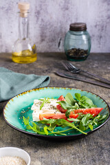 Fresh appetizer of tomatoes, feta cheese and arugula on a plate. Organic diet. Vertical view