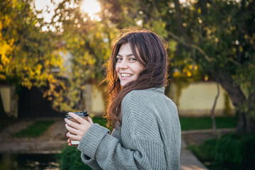 A young woman in a sweater with a cup of coffee in nature.