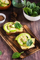 Rye bread bruschetta with avocado, cheese, spinach and flax seeds on a board. Healthy food. Vertical