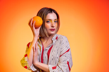 Beautiful attractive blond young woman light blue eyes holding orange with bright yellow background - Studio photography of pretty happy woman holds citrus in hands