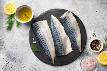 Raw fresh fillet mackerel fish with aromatic herbs, spices, lemon and olive oil on grey background. Healthy food and diet concept.