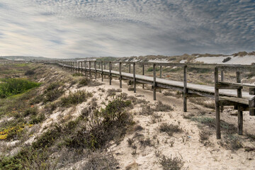 Long wooden bridge over white sand dunes on Costa Nova, Portugal. Sky full of clouds. High quality photo