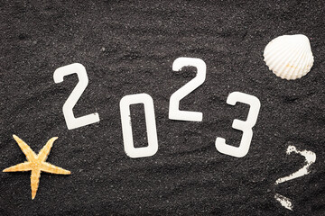 Concept de bonne année 2023 avec un coquillage et une étoile de mer sur du sable de plage noir....