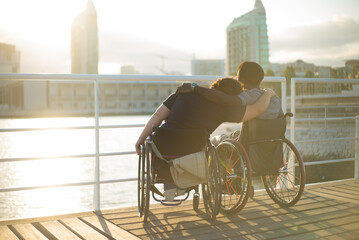 Calm biracial family having romantic date. African American man and Caucasian woman in wheelchairs, leaning on shoulder, looking at sunset. Love, affection, happiness concept